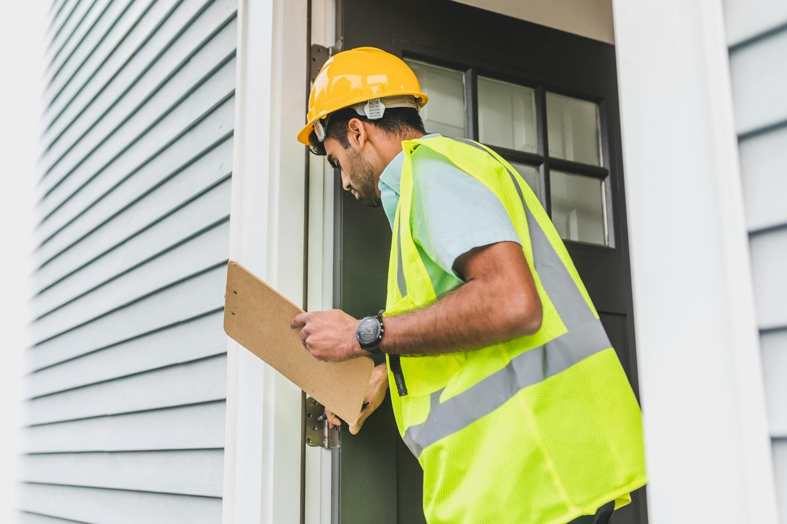 Roofer on ladder with clipboard inspecting roof condition